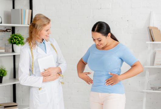 smiling nutritionist holding digital tablet and looking at patient in clinic