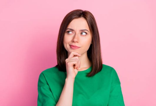 Photo portrait of nice young lady skeptical look empty space not believe doubt dressed trendy green look isolated on pink color background.